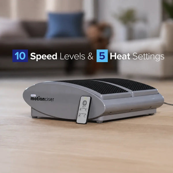 Gray 'motionciser' device with remote control on a wooden surface, blurred living room background.
