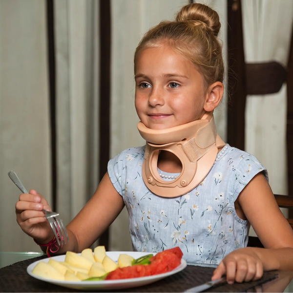 Young girl with a neck brace sitting at a table with a plate of food.